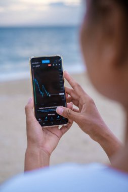 Asian women checking oil prices on their phones when on holiday , women checking their phone on vacation 