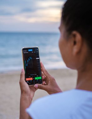 Asian women check Ethereum cryptocurrency on their phone when on holiday , women checking her phone on vacation 