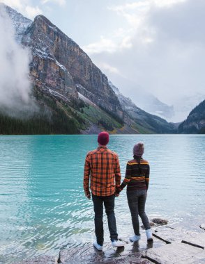 Lake Louise Banff national park, is a lake in the Canadian Rocky Mountains. A young couple of men and women standing by the lake during a cold day in Autumn in Canada