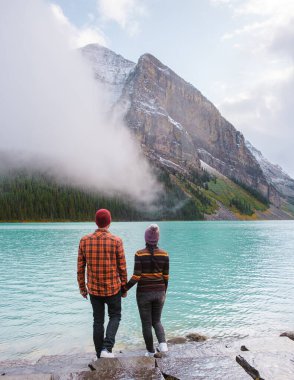 Lake Louise Banff national park, is a lake in the Canadian Rocky Mountains. A young couple of men and women standing by the lake during a cold day in Autumn in Canada