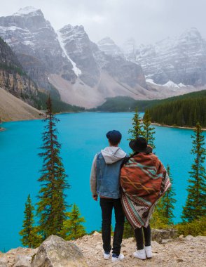  Lake moraine during a cold snowy day in Canada, turquoise waters of the Moraine lake with snow. Banff National Park of Canada Canadian Rockies. Young couple men and women standing by the lake