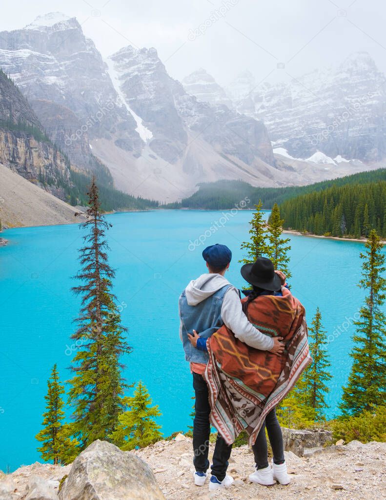  Lake moraine during a cold snowy day in Canada, turquoise waters of the Moraine lake with snow. Banff National Park of Canada Canadian Rockies. Young couple men and women standing by the lake
