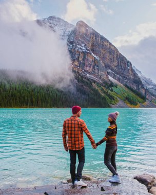 Lake Louise Banff national park, is a lake in the Canadian Rocky Mountains. A young couple of men and women standing by the lake during a cold day in Autumn in Canada