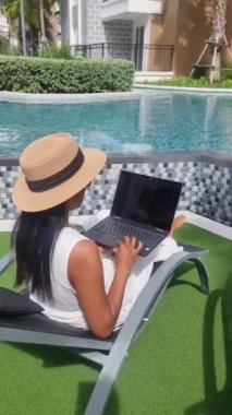 Asian women with hat checking laptop on holiday vacation, digital nomad concept. women with a laptop computer by the pool
