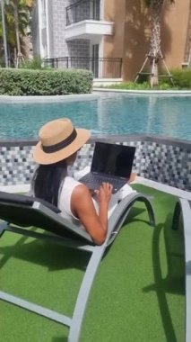 Asian women with hat checking laptop on holiday vacation, digital nomad concept. women with a laptop computer by the pool