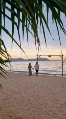 Men and women walking on the beach in Pattaya during sunset in Thailand Ban Amphur beach. couple walking on a tropical beach with palm tree and hammock during sunset