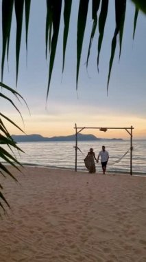 Men and women walking on the beach in Pattaya during sunset in Thailand Ban Amphur beach. couple walking on a tropical beach with palm tree and hammock during sunset