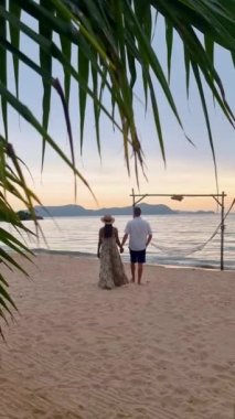 Men and women walking on the beach in Pattaya during sunset in Thailand Ban Amphur beach. couple walking on a tropical beach with palm tree and hammock during sunset