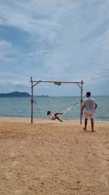 Men and women are relaxing in hammocks on the Pattaya Thailand Ban Amphur beach. couple walking on a tropical beach with palm tree and hammock during sunset