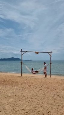 Men and women are relaxing in hammocks on the Pattaya Thailand Ban Amphur beach. couple walking on a tropical beach with palm tree and hammock during sunset