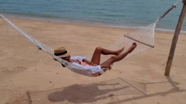 Women are relaxing in a hammock on the beach in Pattaya in Thailand Ban Amphur beach. women walking on a tropical beach with palm trees and hammocks