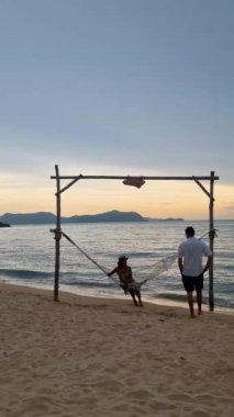 Men and women walk on Pattaya beach during sunset in Thailand Ban Amphur beach with hammock. couple walking on a tropical beach with palm tree and hammock during sunset