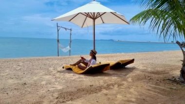 Women on a beach bed on the beach in Pattaya in Thailand Ban Amphur beach. women walking on a tropical beach with palm tree and hammock
