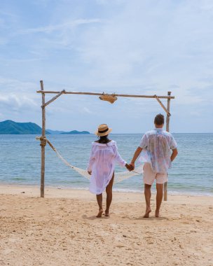 Men and women on the beach on a sunny day with a hammock on beach in Pattaya Thailand Ban Amphur beach. couple walking on a tropical beach with palm trees and hammock 