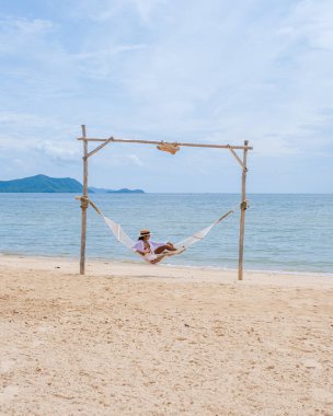 Women on the beach on a sunny day with a hammock on the beach in Pattaya Thailand Ban Amphur beach. Asian women on a tropical beach with palm trees and hammocks 
