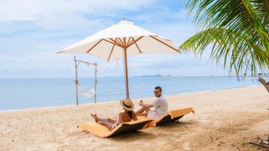 Men and women on the beach are relaxing in a beach chair on a sunny day with a hammock in Pattaya Thailand Ban Amphur beach. couple walking on a tropical beach with palm trees and hammock 