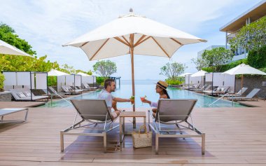 couple men and women relaxing on a beach chair in front of the swimming pool at a luxury vacation, men and women by the pool with a cocktail