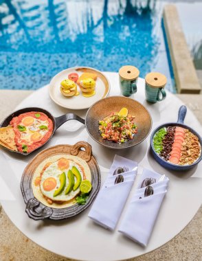 Luxury breakfast by a swimming pool during vacation. Breakfast with eggs and coffee. Poached eggs on a plate, Mexican and Italian style eggs, poached eggs on a plate with avacado