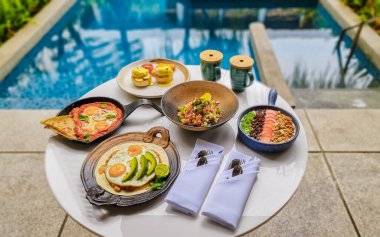 Luxury breakfast by a swimming pool during vacation. Breakfast with eggs and coffee. Poached eggs on a plate, Mexican and Italian style eggs, poached eggs on a plate with avacado