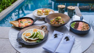 Luxury breakfast by a swimming pool during vacation. Breakfast with eggs and coffee. Poached eggs on a plate, Mexican and Italian style eggs, poached eggs on a plate with avacado