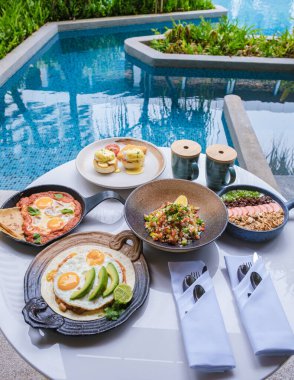 Luxury breakfast by a swimming pool during vacation. Breakfast with eggs and coffee. Poached eggs on a plate, Mexican and Italian style eggs, poached eggs on a plate with avacado