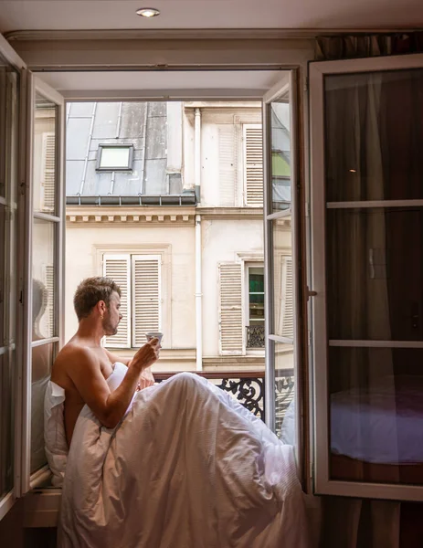 young man sitting in a window looking out over the city of Paris. Men enjoy the sun in the window of a hotel room. Men in the morning by the window in the bedroom