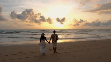 Men and women walking on the beach during sunset in Phuket Thailand. Asian women and European men walking on the beach at sunset 