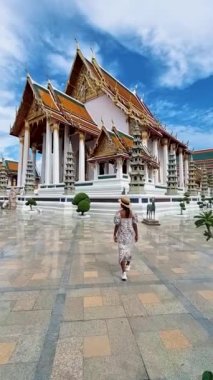 Bangkok Tayland, Wat Suthat Thepwararam Ratchaworahawihan tapınağı eski Bangkok şehrinde. Asyalı kadın ve Avrupalı erkekler sıcak bir günde Bangkok 'ta bir tapınağın önünden geçiyorlar.