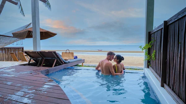 夕阳西下时 一对情侣在豪华别墅的游泳池里欣赏着大海和海滩上的美景 男人和女人正在休假看日落 — 图库照片
