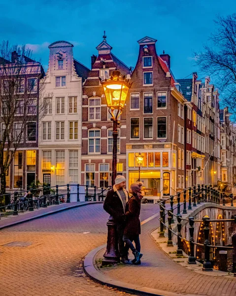 Amsterdam at night couple men and women on a city trip in Amsterdam, Amsterdam at night with dancing colorful house at the Amsterdam canals in the Netherlands.