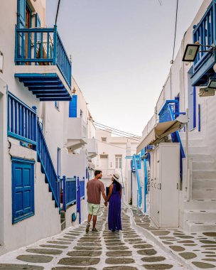 Mykonos Yunanistan 'da tatilde, iki erkek ve kadın beyaz boyalı binalarla Mykonos' u ziyaret ediyorlar. Genç çift Mykonos Yunanistan 'da güneşin doğuşunu izliyor