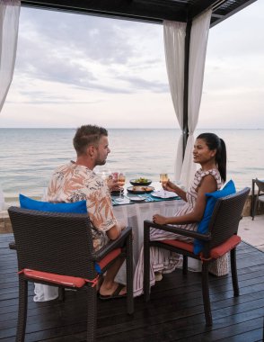 Tayland sahilinde mum ışığında akşam yemeği. Sahilde romantik bir akşam yemeği. Birkaç erkek ve kadın sahilde yemek yiyor.