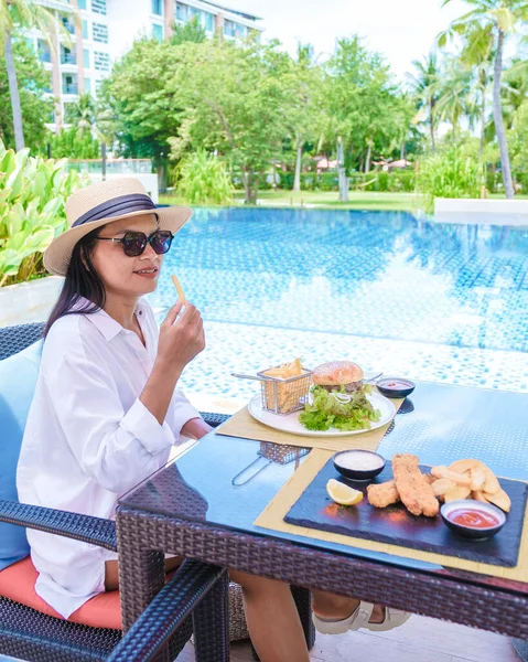 アジアの女性はハンバーガーと魚とチップでプールで昼食を取っています — ストック写真