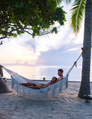 Hua Hin Tayland 'da tropik bir plajda güneşin doğuşunu izleyen bir çift kadın ve erkek. Huahin Tayland sahilindeki hamakta Asyalı kadınlar ve Avrupalı erkekler