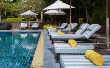 Lüks bir tatil köyünde palmiye ağaçları ve plaj sandalyeleri olan tropik bir havuz, okyanusa bakan palmiye ağaçları olan bir havuz. Havuzda plaj havlusu olan plaj sandalyeleri
