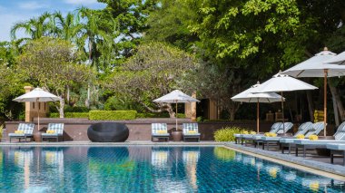 Lüks bir tatil köyünde palmiye ağaçları ve plaj sandalyeleri olan tropik bir havuz, okyanusa bakan palmiye ağaçları olan bir havuz. Havuzda plaj havlusu olan plaj sandalyeleri