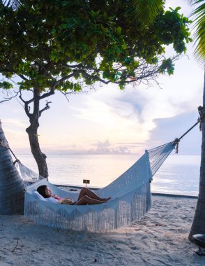 Tayland Hua Hin 'deki tropik bir sahilde palmiye ağaçlarının altında gün doğumunu izleyen kadınlar. Huahin 'deki tropik plajda, okyanus kıyısında beyaz bir plajda hamak var.