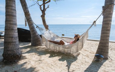 Hua Hin Tayland 'da tropik bir plajda güneşin doğuşunu izleyen bir çift kadın ve erkek. Huahin Tayland sahilindeki hamakta Asyalı kadınlar ve Avrupalı erkekler