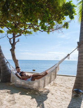 Hua Hin Tayland 'da tropik bir plajda güneşin doğuşunu izleyen bir çift kadın ve erkek. Huahin Tayland sahilindeki hamakta Asyalı kadınlar ve Avrupalı erkekler