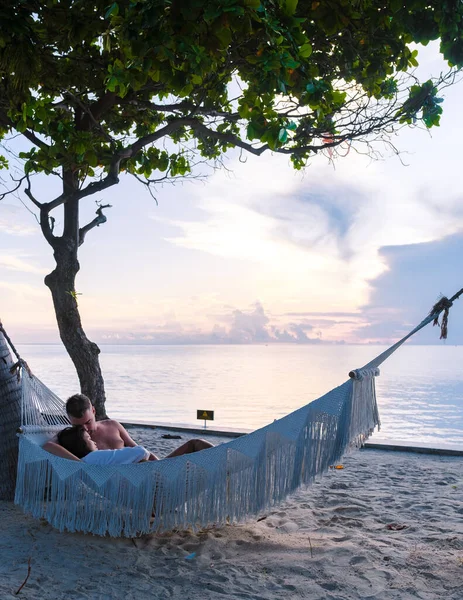 Couple of men and women watching the sunrise in a hammock on a tropical beach in Hua Hin Thailand. Asian women and European men in a hammock on the beach of Huahin Thailand