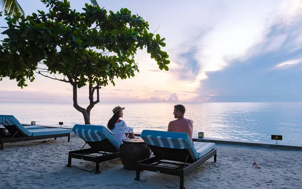 Couple of men and women relaxing by the pool in beach beds chairs, tropical pool, pool with palm trees at the beach looking out over the ocean