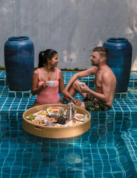 A couple having breakfast in the swimming pool , Asian women and Caucasian men having floating breakfast in the pool