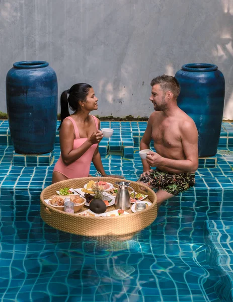 A couple having breakfast in the swimming pool , Asian women and Caucasian men having floating breakfast in the pool