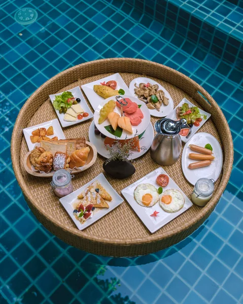 Top view of floating breakfast in the swimming pool, floating breakfast in the pool with bread eggs and fruit, and coffee