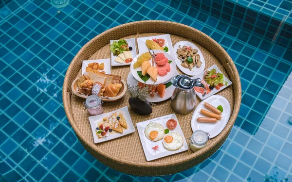 Top view of floating breakfast in the swimming pool, floating breakfast in the pool with bread eggs and fruit, and coffee