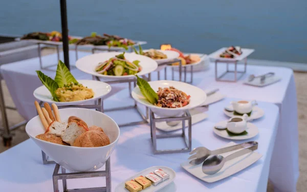 Buffet table by the ocean with fresh salad and bread and Thai food