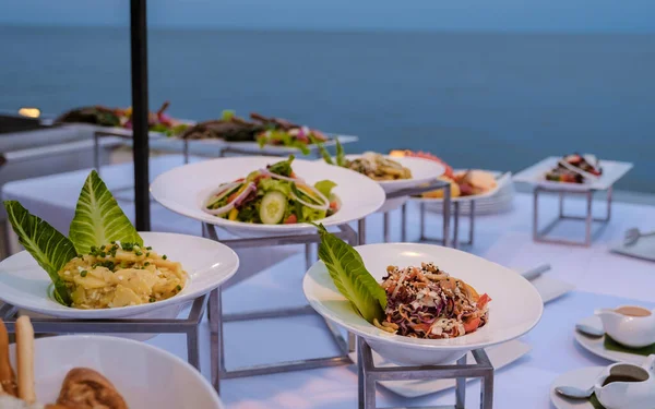 Buffet table by the ocean with fresh salad and bread and Thai food