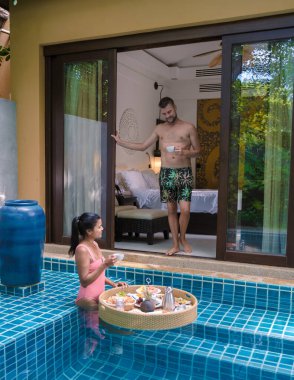 Yüzme havuzunda kahvaltı yapan bir çift, Asyalı kadınlar ve beyaz erkekler havuzda yüzen kahvaltı yapıyorlar.