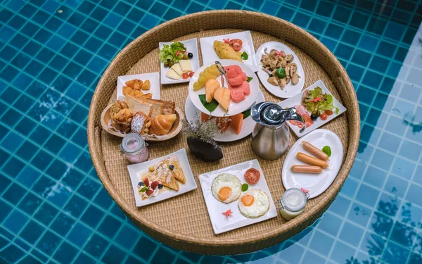 Top view of floating breakfast in the swimming pool, floating breakfast in the pool with bread eggs and fruit, and coffee