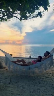 Hua Hin Tayland 'da tropik bir plajda güneşin doğuşunu izleyen bir çift kadın ve erkek. Huahin Tayland sahilindeki hamakta Asyalı kadınlar ve Avrupalı erkekler